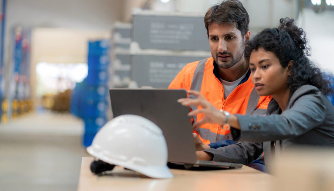 Warehouse manager and inventory controller analyzing stock data using a computer. Business strategy, supply chain efficiency, and warehouse management optimization. Logistics, teamwork, freight transportation, and digital transformation in a distribution warehouse.